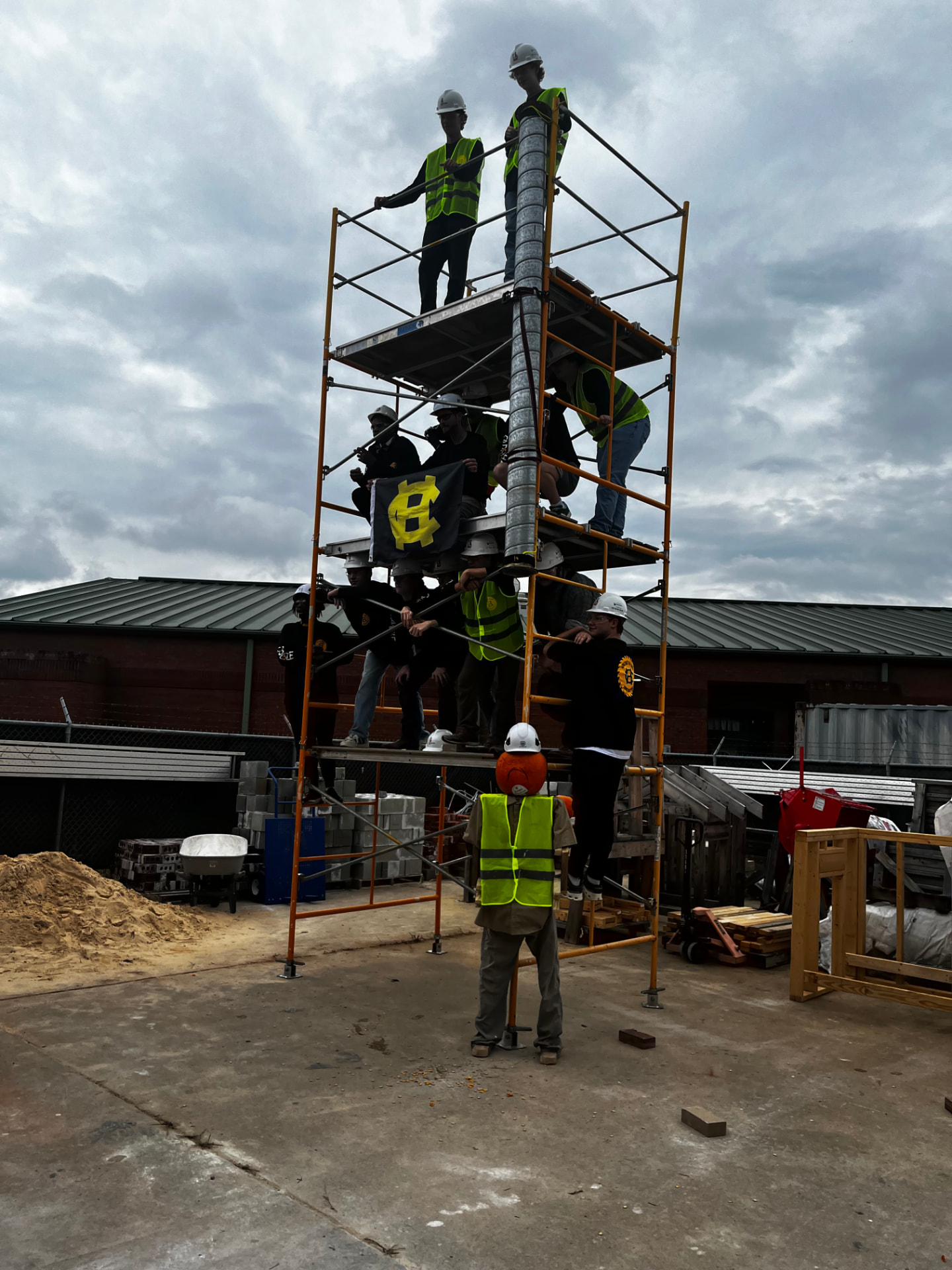 Construction students in hard hats and safety vests on a tall scaffolding tower