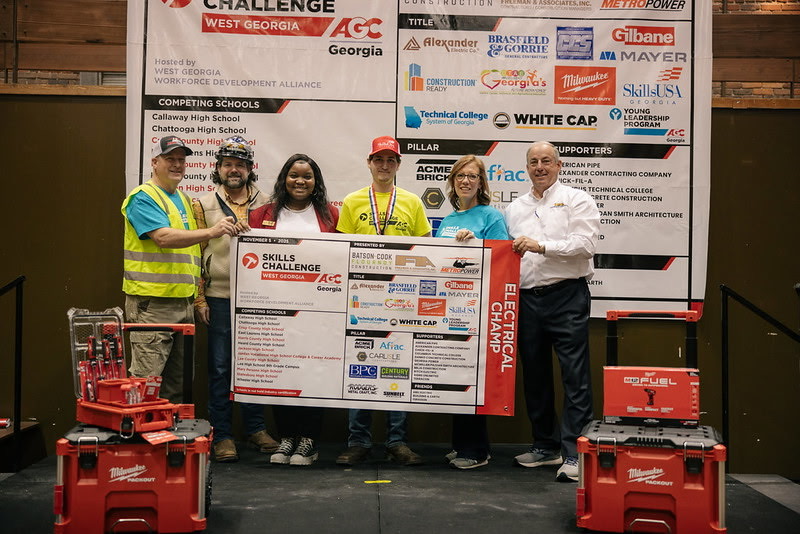 Hayden holding the AGC Georgia Skills Challenge Electrical Champ banner with industry representatives